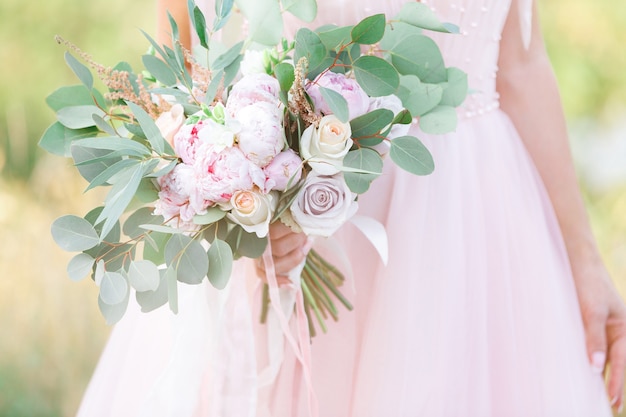 Die Hände der Braut halten einen schönen Rosenstrauß. Kunstfotografie.