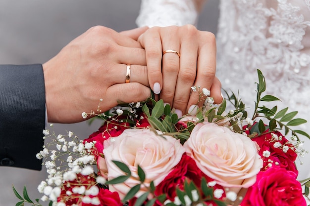 Die Hände der Braut und des Bräutigams mit Ringen auf dem Hintergrund eines Hochzeitsbouquets mit Rosen Das Konzept der Ehe