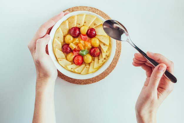 Die Hände der Draufsichtfrau, die Morgenbrei mit Äpfeln, Kirschen und kandierten Früchten auf weißem Hintergrund essen