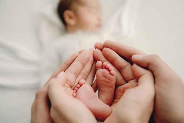 Die Hände der Eltern halten winzige Füße des neugeborenen Jungen in der Nähe, während er schläft. Familienporträt mit süßem Kleinkind, das ein Nickerchen macht