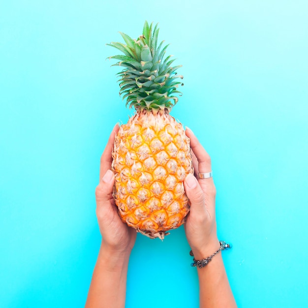 Die Hände der Frau, die Ananas auf blauem Farbhintergrund halten