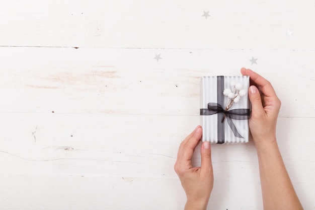 Die Hände der Frau, die ein schönes Weihnachtsgeschenk halten, das in gestreiftem Papier mit Schleife verpackt ist