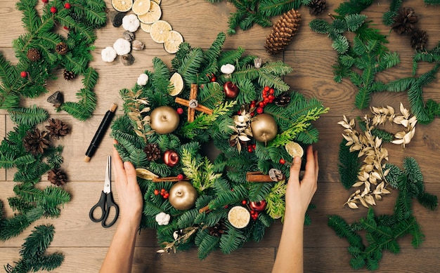 Die Hände der Frau, die einen handgemachten Weihnachtskranz halten. Neujahrsfeiertagsdekoration, Weihnachtsbaumkranzdekoration mit den Händen der Frauen DIY.