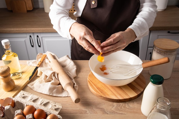 Die Hände der Frau gießen das zerbrochene Ei in eine Schüssel Milch, um den hausgemachten Teig zum Backen weiter vorzubereiten. Küche.