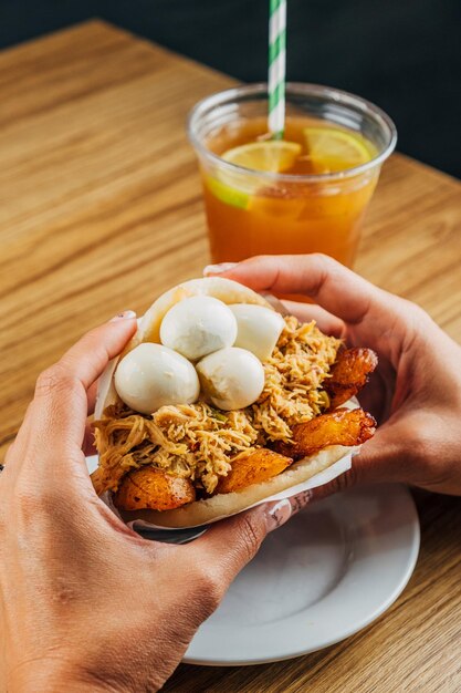 Foto die hände der frau halten köstliche venezolanische arepa, gefüllt mit huhn, gebratener bananen und corniz-eiern