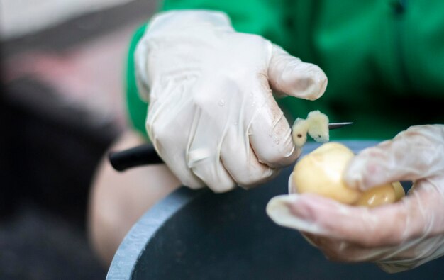 Die Hände der Frau in weißen Handschuhen schälen rohe neue Kartoffeln in der Nähe Reinigung von Bio-Kartoffeln