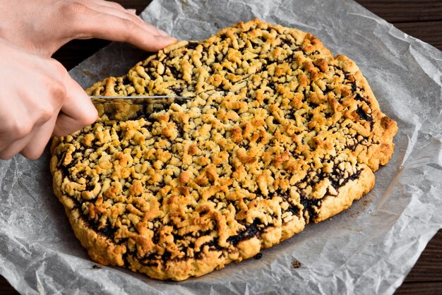 Die Hände der Frau schneiden Obstkuchen Kuchen auf einem Holztisch