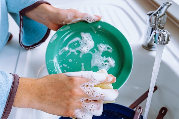 Die Hände der Frau waschen Teller in der Küchenspüle