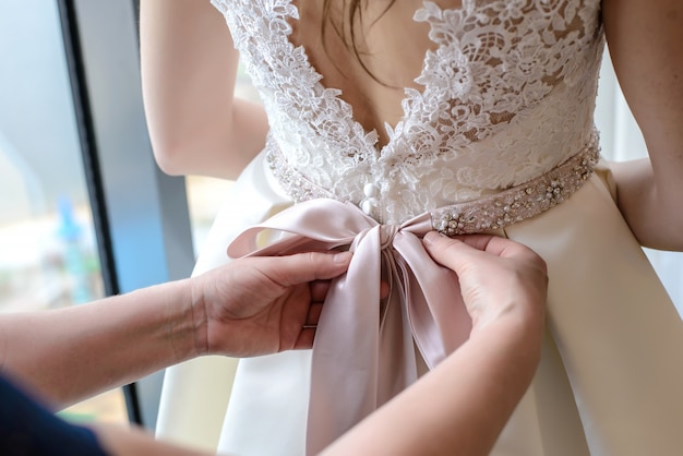 Die Hände der Frauen binden Bogen auf Brautkleid