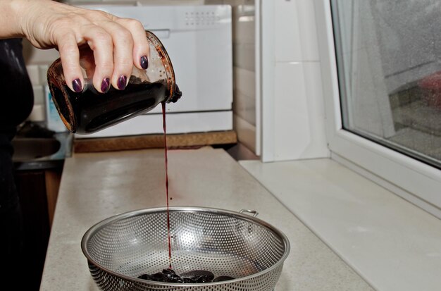 Foto die hände der frauen gießen marmelade aus einer dose in eine schüssel durch ein sieb vor dem hintergrund des kücheninterieurs beim kochen