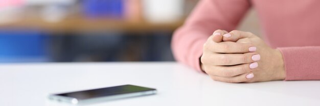 Die Hände der Frauen liegen auf dem Tisch in der Nähe des Mobiltelefons, das auf das Anrufkonzept wartet