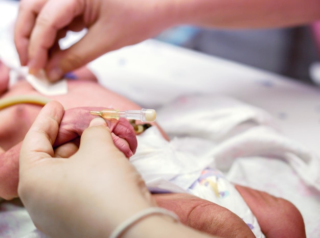 Die Hände der Krankenschwester stechen einem kranken Neugeborenen einen Injektionsstecker in die Hand, um Füllmedikamente vorzubereiten