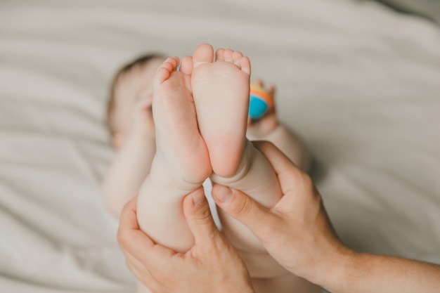 Die Hände der Mutter halten die Beine des Babys auf einem Baumwollbett. Hygiene und Pflege und Pflege der Ferse des Neugeborenen