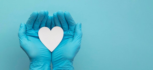 Foto die hände des arztes tragen blaue op-handschuhe, die eine weiße herzform halten