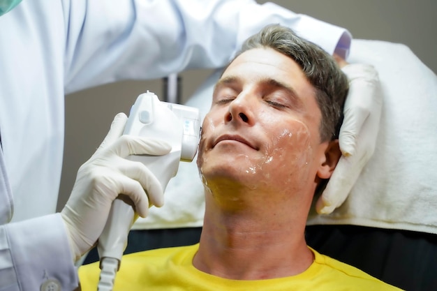 Die Hände des Arztes verwenden eine Farblicht-Gesichtsstimulatortherapie, um das Wohlbefinden der Gesichtshaut zu stimulieren