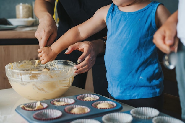 Die Hände des Babys machen Muffins, die rohen Teig in Formen gießen Glücklicher Familientag