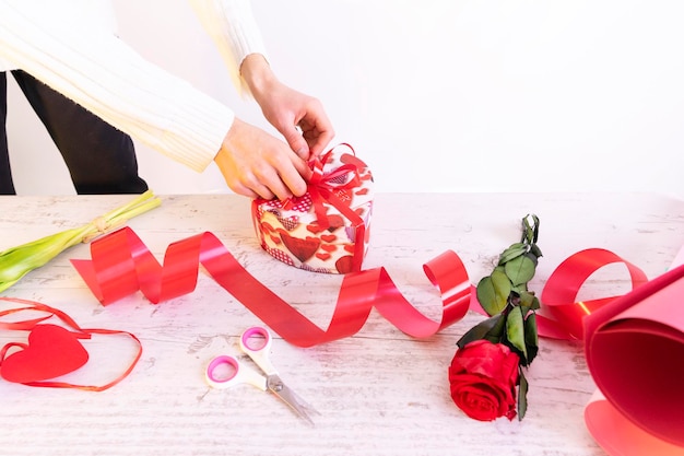 Die Hände des Floristenverkäufers schmücken die Geschenkbox mit Band auf dem Packtisch mit einer Bandschere und einer Rose im ShopEin romantisches Geschenk mit Ihren eigenen Händen