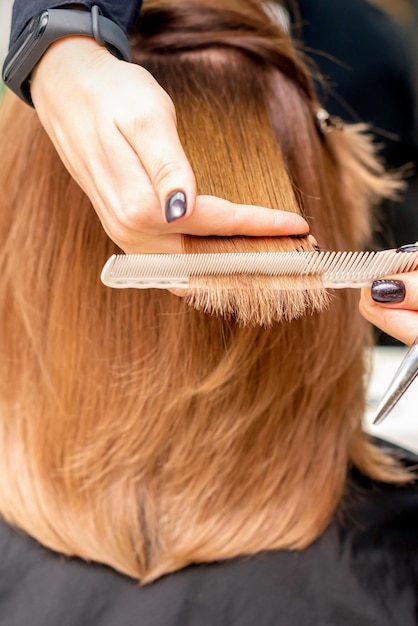 Die Hände des Friseurs halten die Haarsträhne zwischen den Fingern und machen einen Haarschnitt der langen Haare der jungen Frau mit Kamm und Schere im Friseursalon aus nächster Nähe