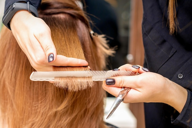 Die Hände des Friseurs halten die Haarsträhne zwischen den Fingern und machen einen Haarschnitt der langen Haare der jungen Frau mit Kamm und Schere im Friseursalon aus nächster Nähe