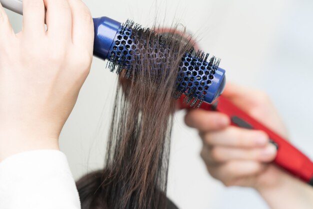 Die Hände des Friseurs trocknen brünette Haare des Kunden mit blauer Haarbürste und rotem Haartrockner im professionellen Schönheitssalon.