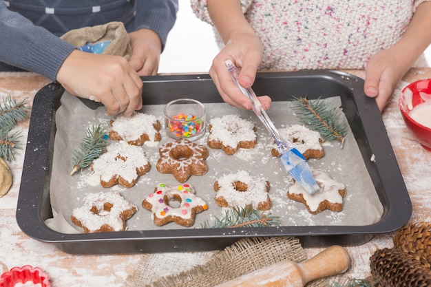 Die Hände des Jungen und des Mädchens schmücken Weihnachtsplätzchen