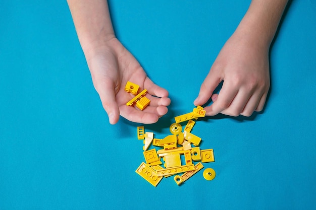 Die Hände des Kindes des Jungen sammeln, falten, spielen mit dem Designer kleine Details in gelber Farbe auf blauem Hintergrund, Anti-Stress