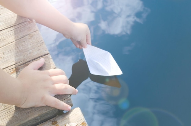 Die Hände des kleinen Jungen lassen sich an sonnigen Tagen in das Wasserpapierboot mit Holzsteg frei