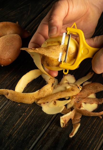 Die Hände des Koch in Nahaufnahme schälen rohe Kartoffeln mit einem Kartoffelschälter, um ein nationales Gericht oder Pommes Frites vorzubereiten.
