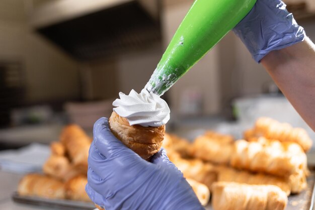 Die Hände des Konditors füllen eine Tube süßen Blätterteig mit geschlagenem Eiweiß und Vanillesoße. Kleine Tortillas in der Backsektion Bäckereiproduktion