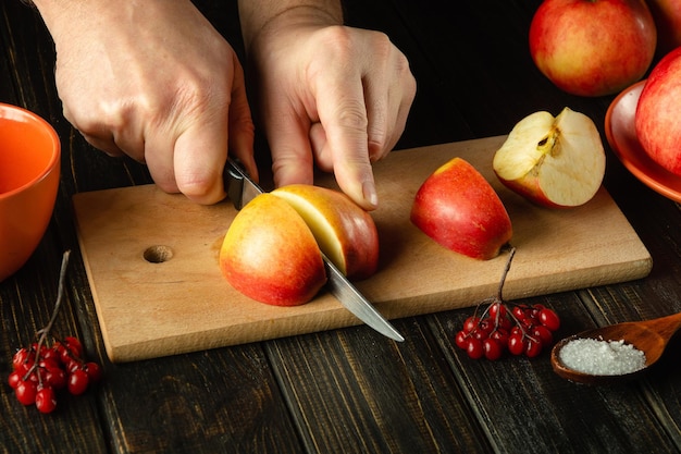 Die Hände des Küchenchefs auf dem Küchentisch schneiden mit einem Messer frische Äpfel auf einem Küchenbrett, um süße Marmelade zuzubereiten