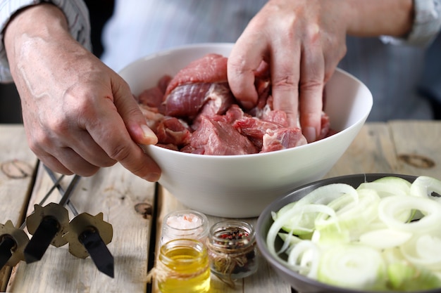 Die Hände des Küchenchefs bereiten Fleischspiesse mit Zwiebeln zu. Eine Schüssel rohes Fleisch und eine Schüssel Zwiebeln. Grillen kochen.