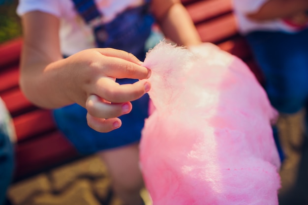 Die Hände des Mädchens, das rosa Zuckerwatte im Hintergrund des blauen Himmels hält