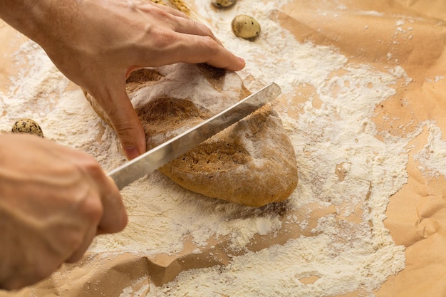 Die Hände des Mannes schneiden ein frisches Weizenbrötchen mit einem Brotmesser