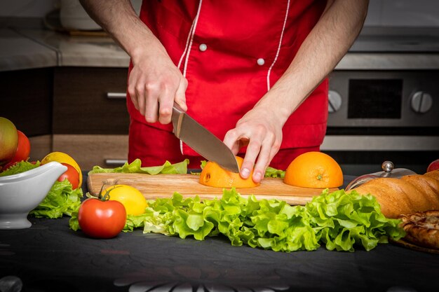 Die Hände des Mannes schneiden frische Orange auf der Küche. Weicher Fokus