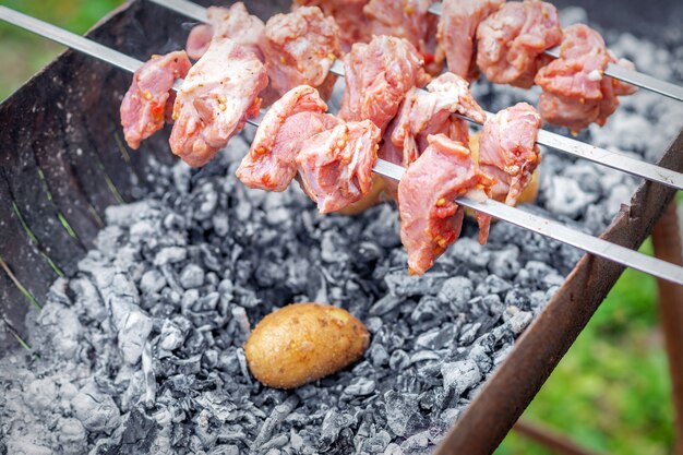 Die hände des menschen bereiten grillfleisch mit kartoffeln am spieß vom grill im freien zu. konzept der rustikalen lebensmittelzubereitung des lebensstils