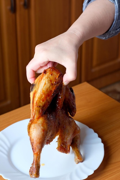 Die Hände einer älteren Frau bedienen ein gegrilltes Hähnchen und stellen es in der Küche an einem braunen Tisch ohne Gesichtsnahaufnahme zur Schau