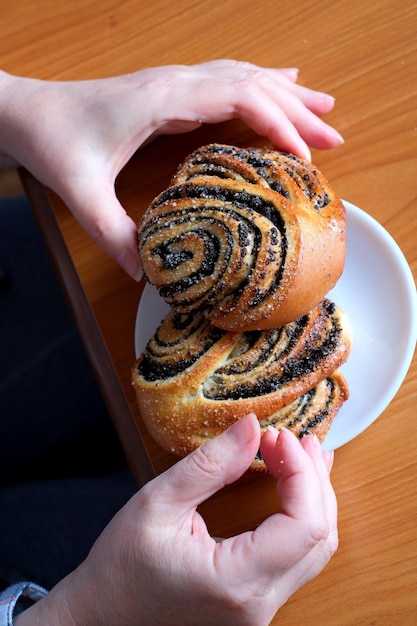 Die Hände einer älteren Frau bedienen in der Küche an einem braunen Tisch ohne Gesichtsnahaufnahme ein süßes Brötchen mit Mohn