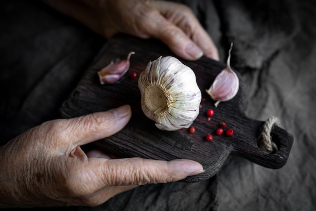 Die Hände einer älteren Frau halten ein Schneidebrett mit Knoblauch aus nächster Nähe