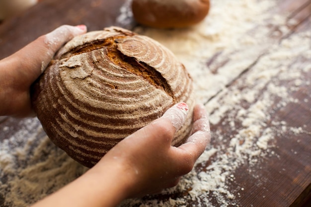 Die Hände einer Frau nehmen frisches, gebrochenes Brot vom mit Mehl bestreuten Holztisch