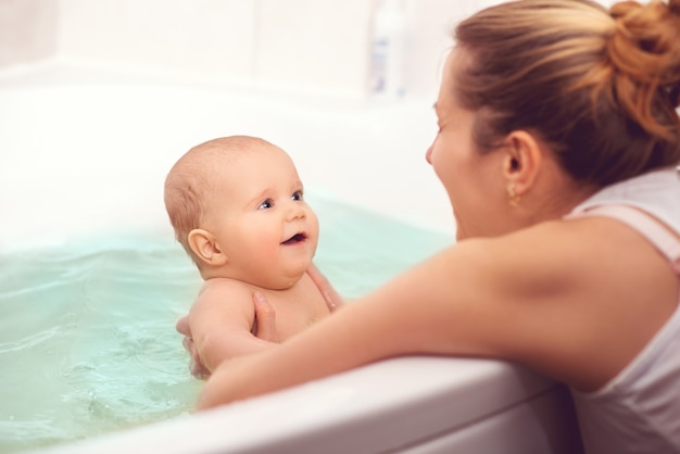 Die Hände einer vorsichtigen Mutter halten ein kleines schönes lustiges Baby mit großen Augen