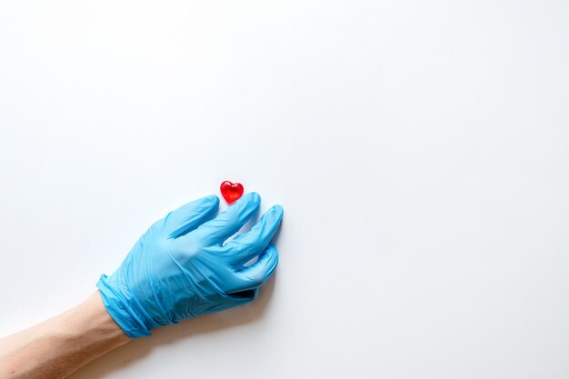 Die Hände eines Arztes in medizinischen Handschuhen auf einer weißen Oberfläche halten Stein in Form eines Herzens