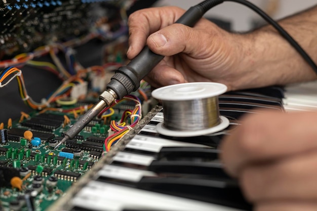 Die Hände eines Elektronikers reparieren den Stromkreis eines Klaviers mit einem Lötkolben