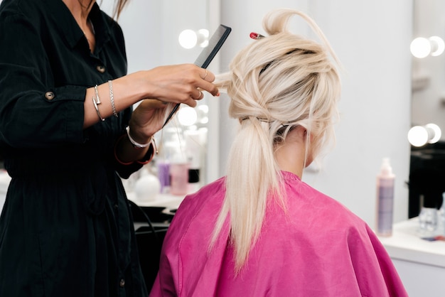 Die Hände eines Friseurs machen eine Frisur für ein blondes Mädchen