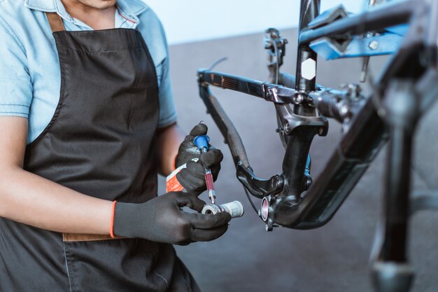 Die Hände eines jungen Mechanikers mit Handschuhen, der das mit Öl zu schmierende Tretlager hält