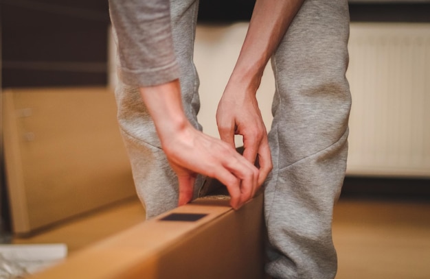 Die Hände eines kaukasischen jungen Mannes öffnen einen großen Karton in seinem Zimmer