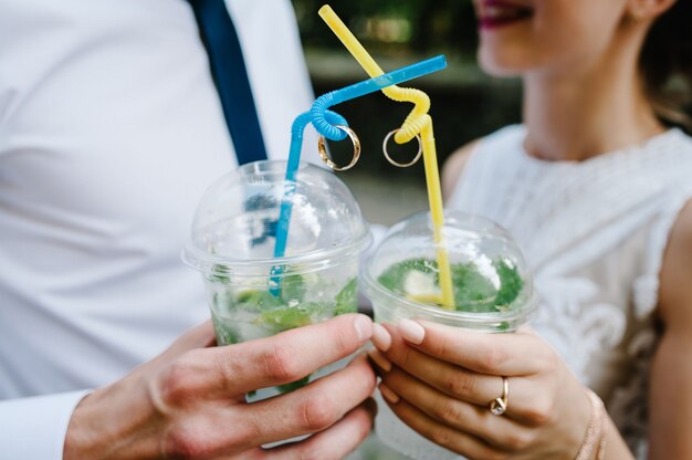 Die Hände eines Mannes und einer Frau halten Plastikgläser Wein oder Champagner und zwei Eheringe