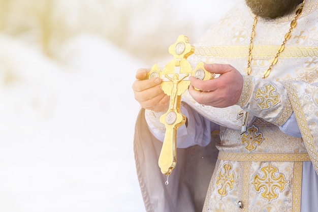 Die Hände eines Priesters tauchen ein orthodoxes Goldkreuz in den Fluss. Fest der Offenbarung Russlands.