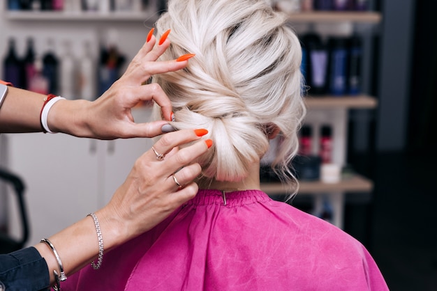 Die Hände eines professionellen Friseurs machen eine Frisur für ein blondes Mädchen mit langen Haaren