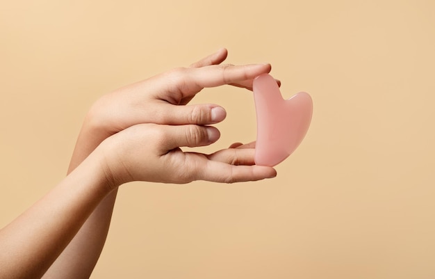 Die Hände zeigen elegant das rosa Rosenquarz-Gua-Sha-Werkzeug im Gesicht in Herzform