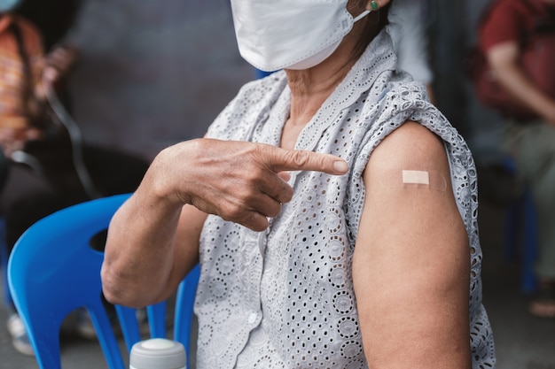 Die Hand der älteren Frau, die mit einem Verband auf die Schulter zeigt, nachdem sie Coronavirus covid geimpft hat